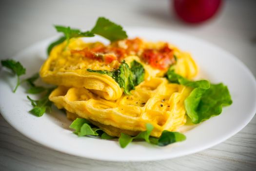 Egg omelet stuffed with tomato and greens fried in the form of waffles, on a wooden table.