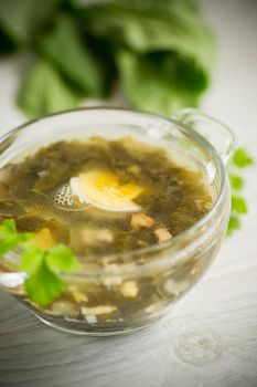 Spring soup from fresh sorrel with boiled eggs in a plate on a wooden table