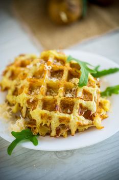 fried potato waffles with cheese in a plate on a light wooden table.