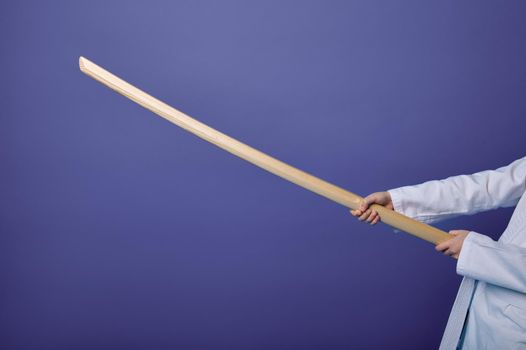 Cropped view of aikido fighter's hands holding wooden weapon - sword bokken- practicing Oriental martial arts skills on purple colored background with copy space for advertising text