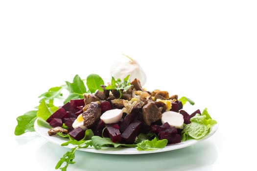 Salad with boiled beets, fried eggplants, herbs and arugula in a plate, isolated on white background.