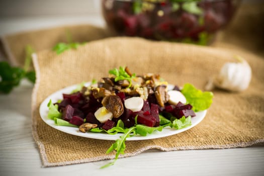 Salad with boiled beets, fried eggplants, herbs and arugula in a plate, on a wooden table.