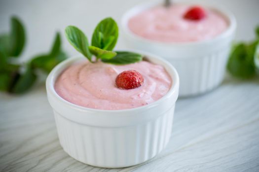 sweet curd mass whipped with fresh strawberries in a bowl, on a wooden table.