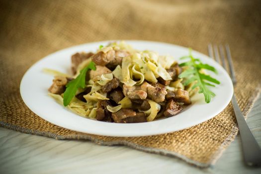 Homemade boiled noodles with meat and eggplant in a plate on a wooden table