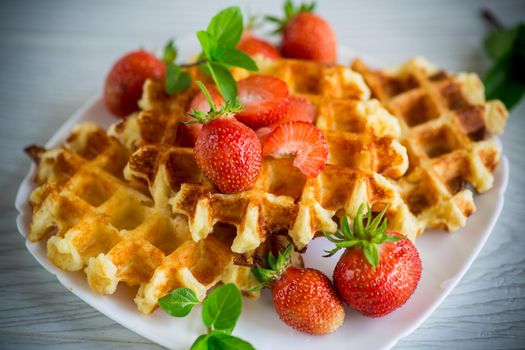 Sweet curd cooked waffles with fresh ripe strawberries, on a wooden table.