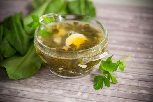 Spring soup from fresh sorrel with boiled eggs in a plate on a wooden table