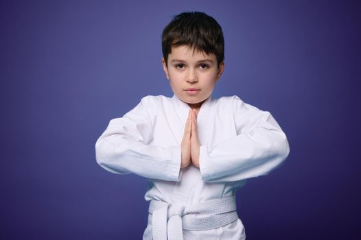 Waist length portrait of a strong European teenage boy, aikido wrestler practicing martial skills against violet wall background with copy space for advertising text. Oriental martial arts concept