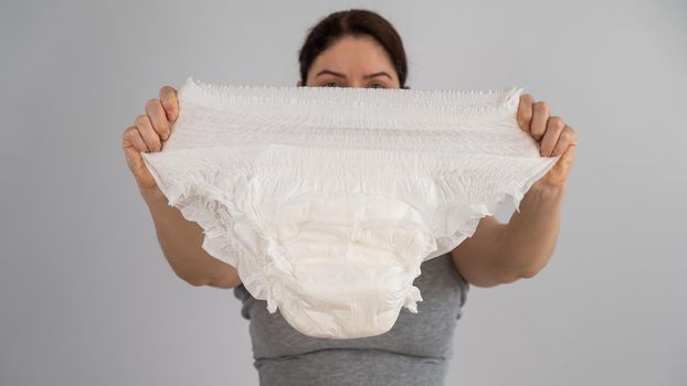 A caucasian woman holds an adult diaper and checks its strength on a white background