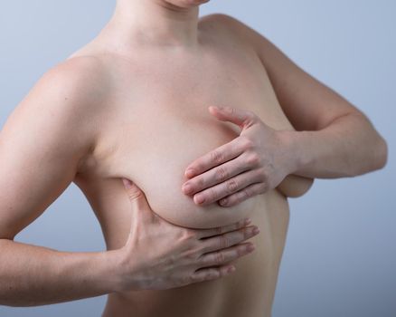 Caucasian woman self checks for breast cancer on white background