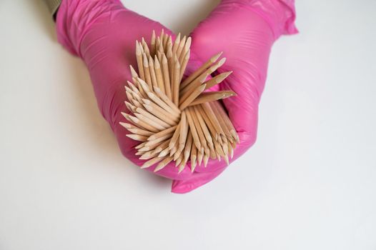 Master in pink gloves holds orange sticks for manicure