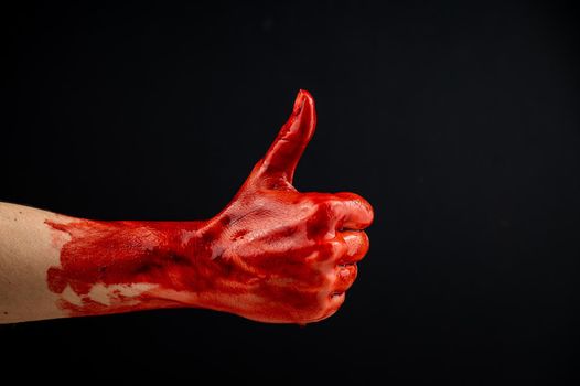 A woman's hand stained with blood shows a thumbs up on a black background