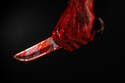 A man with bloody hands brandishes a knife on a black background