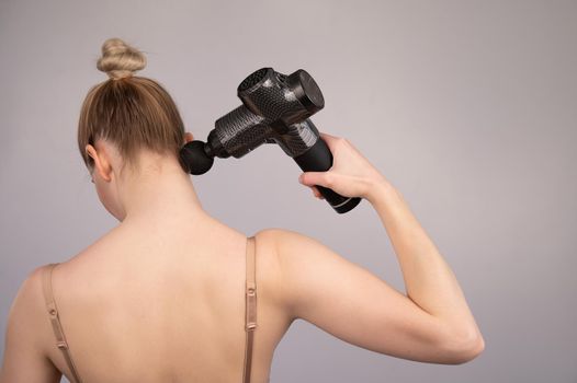 Caucasian woman giving herself a back massage with a gun