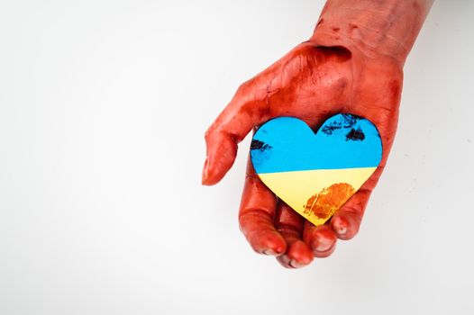 Woman with hands covered in blood holding a heart with the flag of ukraine on a white background. Copy spae