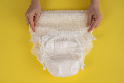 A woman holds an adult diaper on a yellow background. Incontinence problems