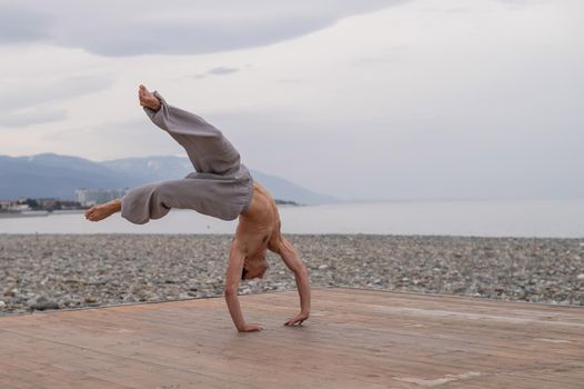 Shirtless caucasian man doing acrobatic wheel on the beach