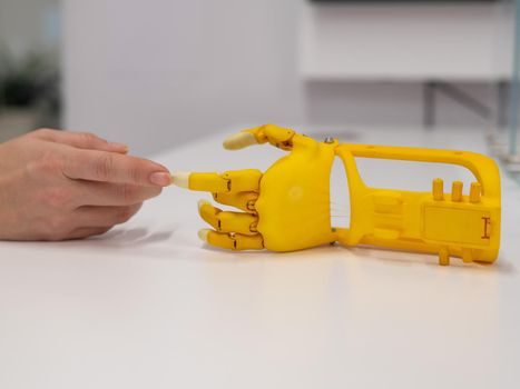 Woman's hand and a plastic hand prosthesis for a child on a white background