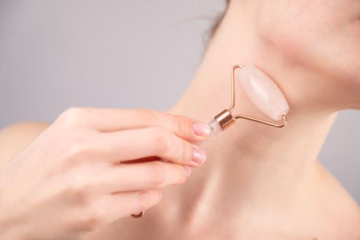 Close-up portrait of a woman using a quartz roller massager for an alternative fight against wrinkles on her neck. Smoothing of the rings of venus