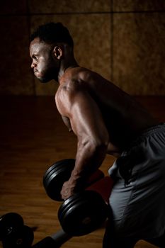 African american man with naked torso doing triceps row with dumbbell on bench