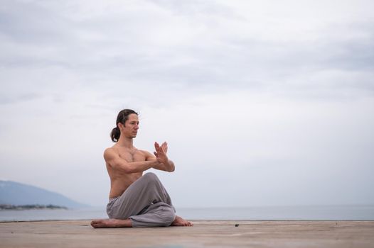 Caucasian man with naked torso practicing wushu on the seashore