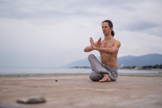 Caucasian man with naked torso practicing wushu on the seashore