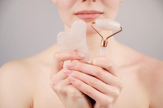 Caucasian woman holding pink roller massager and gouache scraper on white background