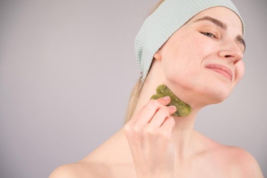 Portrait of a young woman massages her face with a gouache scraper on a white background