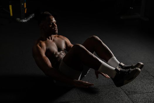 Afro american man doing abdominal exercises in a dark studio