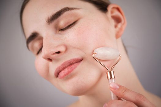 Close-up portrait of a woman using a quartz roller massager on her cheek for an alternative anti-aging