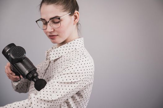 Caucasian business woman massaging her biceps with a percussion massager