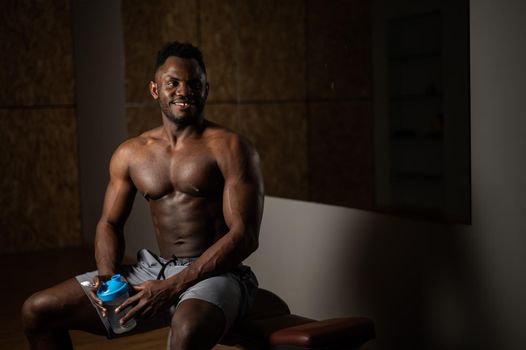 Shirtless african american man drinking from a shaker in the gym