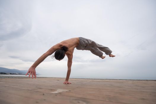 Shirtless caucasian man doing backflip on pebble beach