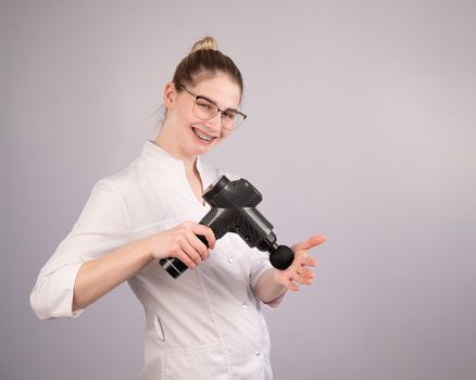 The masseur doctor holds a masseur gun on a white background