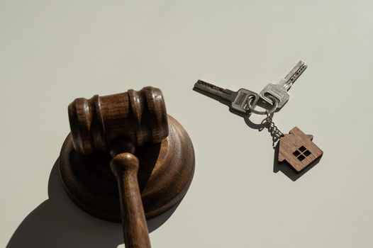 Keys with a keychain in the shape of a house and a judge's gavel on a white background