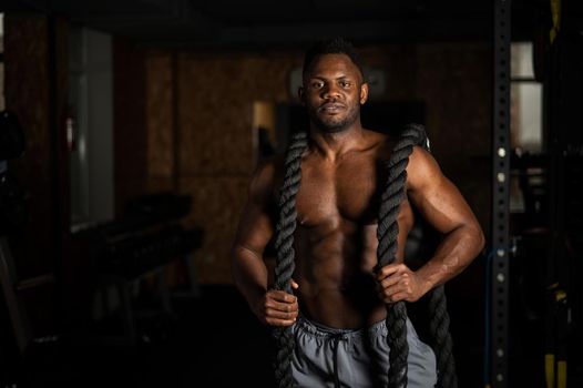 Muscular african american man posing with rope in gym