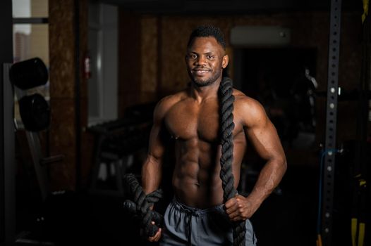 Muscular african american man posing with rope in gym