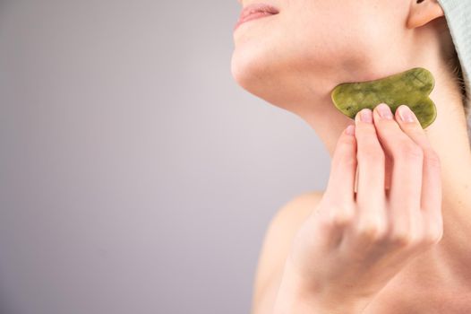 Close-up portrait of a young woman massaging her neck with a gouache scraper