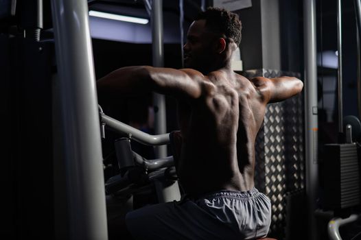 Shirtless african american man doing back exercises on a machine in the gym