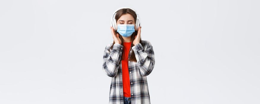 Social distancing, leisure and lifestyle on covid-19, coronavirus concept. Carefree relaxed woman in medical mask carried away with music in headphones, close eyes from satisfaction nice sound.