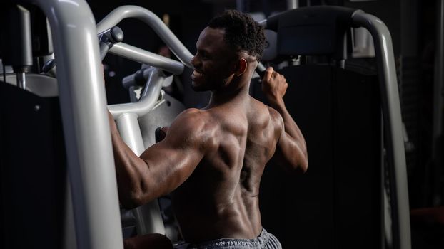 Shirtless african american man doing back exercises on a machine in the gym