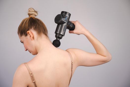 Caucasian woman giving herself a back massage with a gun