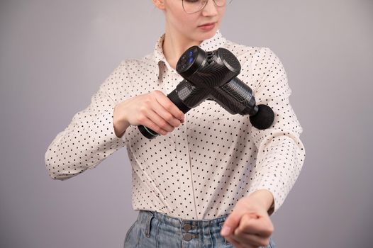 Caucasian business woman massaging her biceps with a percussion massager