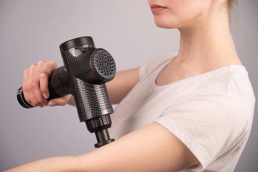 Caucasian woman uses a massager gun for pain in the muscles of the arm