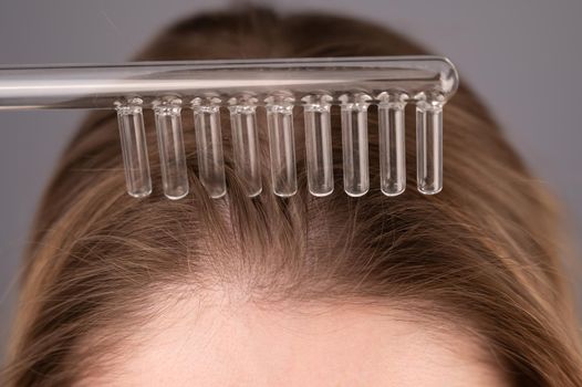 Caucasian woman combing her hair with a darsonval device