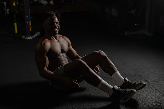 Afro american man doing abdominal exercises in a dark studio