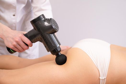 The doctor massages the thigh of the patient with an electric massager with a gun