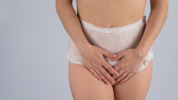 A woman in adult diapers holds her hands on her stomach. Urinary incontinence problem