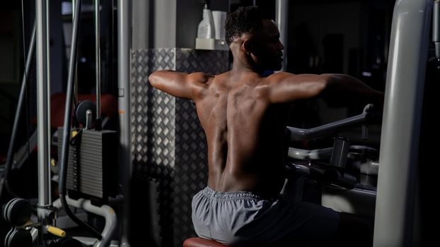 Shirtless african american man doing back exercises on a machine in the gym