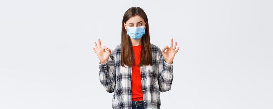 Coronavirus outbreak, leisure on quarantine, social distancing and emotions concept. Determined young woman in medical mask assure all good, show okay signs and wink, no problem.