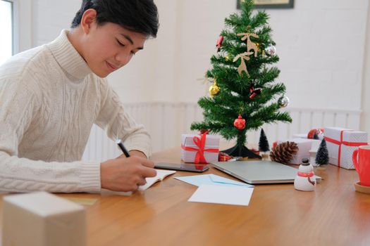man wearing cream sweater writing note on notebook at home during christmas new year holiday celebration.